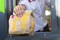 McDonald's worker holding bag of fast food. McDonald's is a mega cap that will have a big Q1.